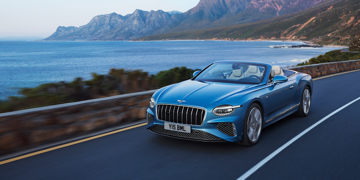 Bentley Bordeaux New Bentley Continental GTC Azure convertible in Light Windsor blue paint with 22 inch Azure wheels and chrome grill, driving dynamically by the sea