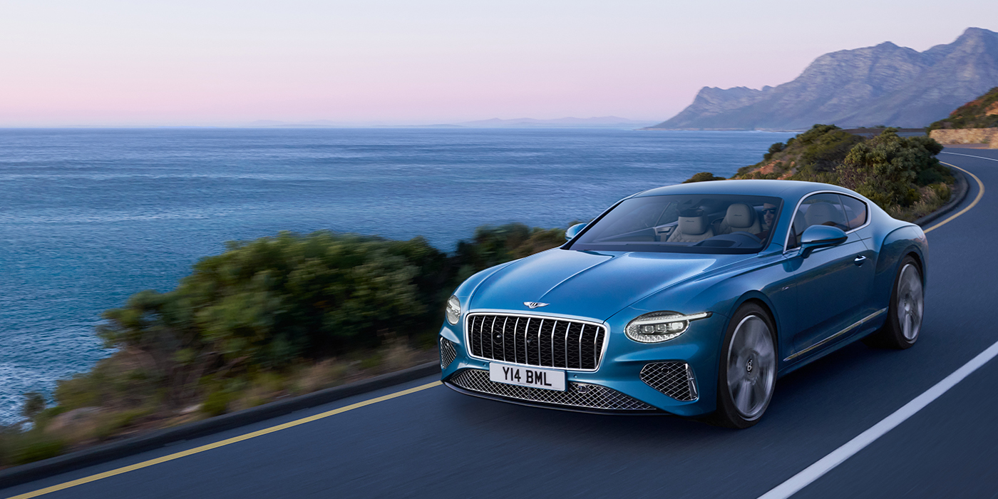 Bentley Bordeaux New Bentley Continental GT Azure coupe in Light Windsor blue paint with 22 inch Azure wheels and chrome grill, driving dynamically by the sea