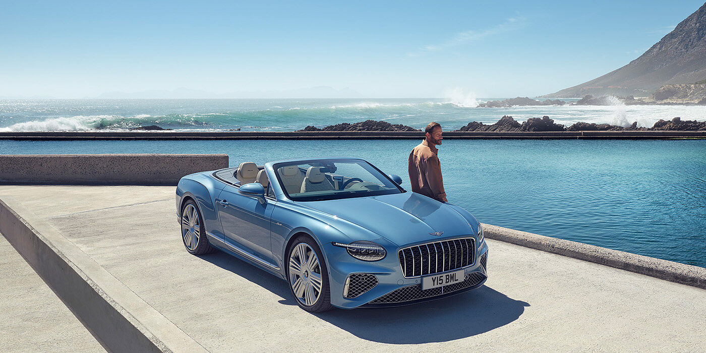 Bentley Bordeaux New Bentley Continental GTC Azure convertible front view in Light Windsor blue paint with 22 inch ten spoke wheels parked by the sea in the sunshine