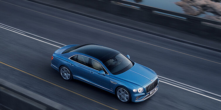 Bentley Bordeaux New Bentley Flying Spur Azure sedan in Light windsor blue paint by Mulliner, with 22 inch Azure wheels seen from overhead driving dynamically on a country road