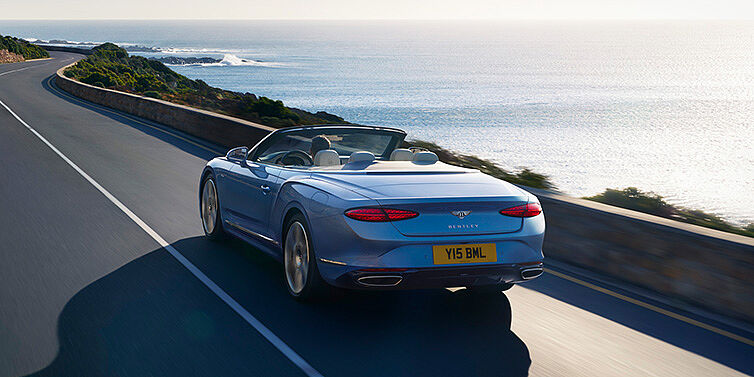 Bentley Bordeaux New Bentley Continental GTC Azure convertible rear view in Light Windsor blue paint with 22 inch ten spoke wheels driving dynamically on an ocean road in the sunshine