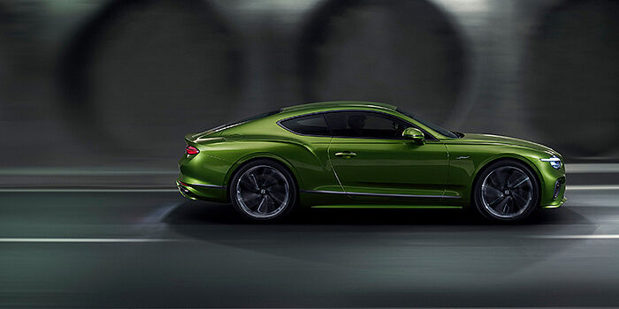  Bentley Bordeaux Bentley Continental GT coupe in Tourmaline Green paint driving in profile on a dark road