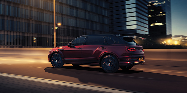 Bentley Bordeaux Bentley Bentayga Extended Wheelbase Mulliner SUV in Cricket Ball red paint driving dynamically in city at night